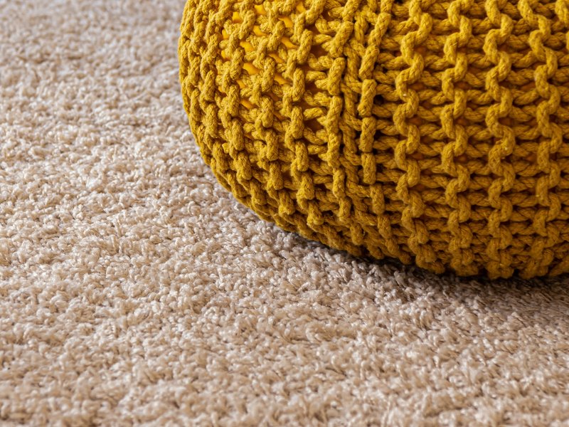 Beige carpet flooring under a yellow ottoman